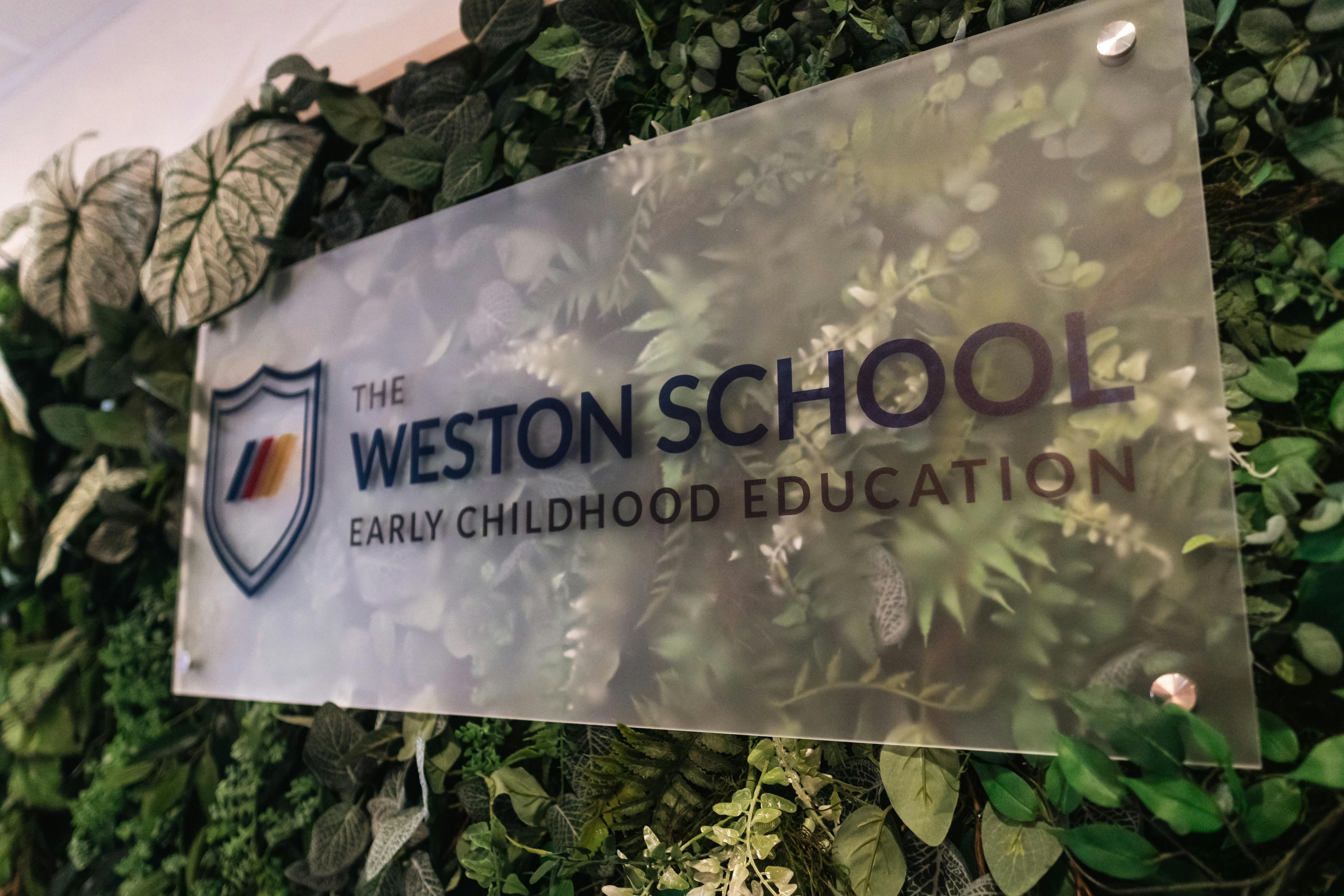 The Weston School Early Childhood Education sign on a green plant wall
