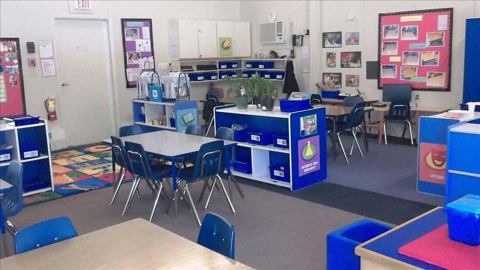 Classroom with small tables and chairs, storage units, and an exit sign above a door
