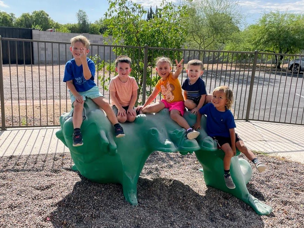 Five children sitting on a green dinosaur playground structure