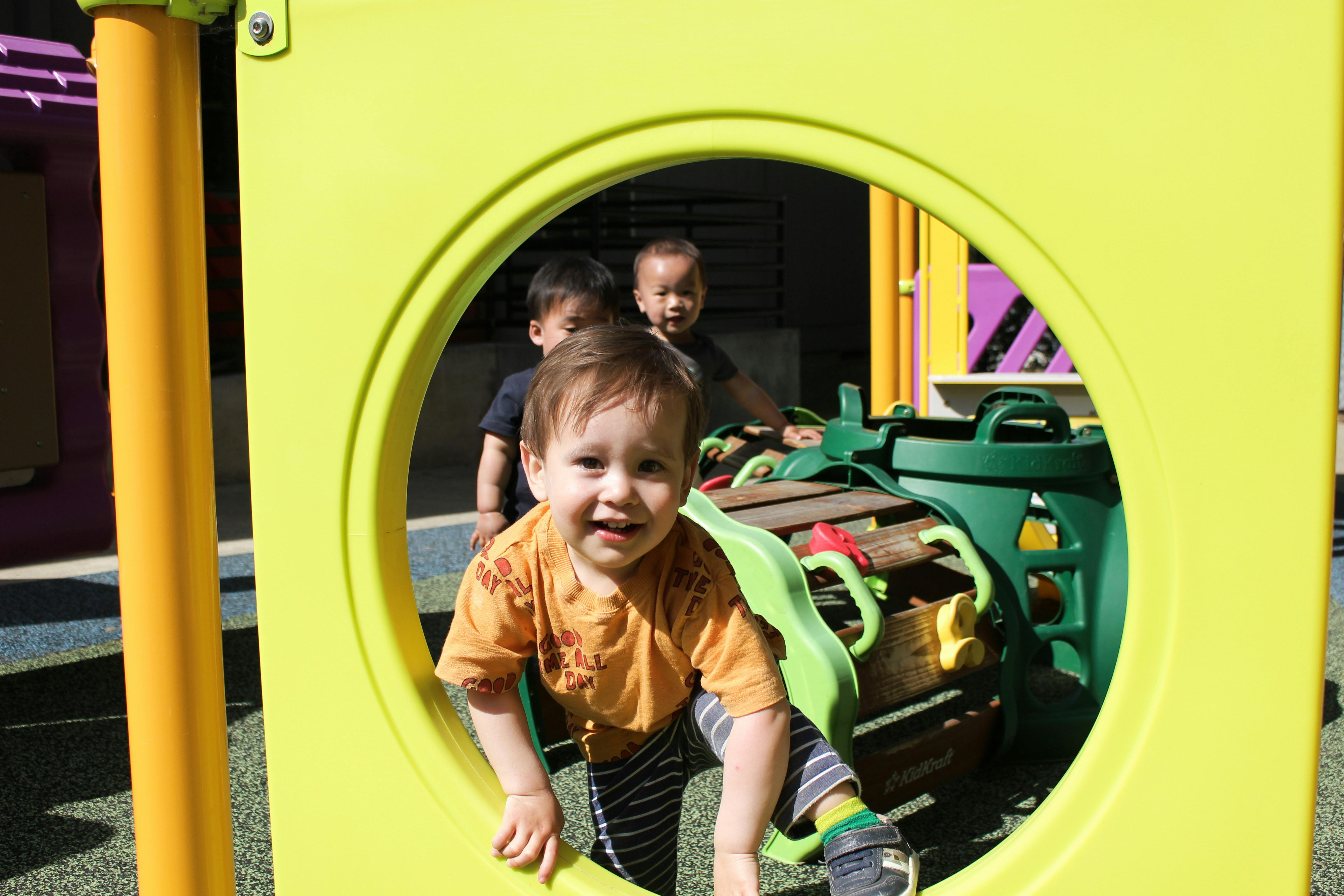 Child looking through a circular opening on a playground structure with other children behind