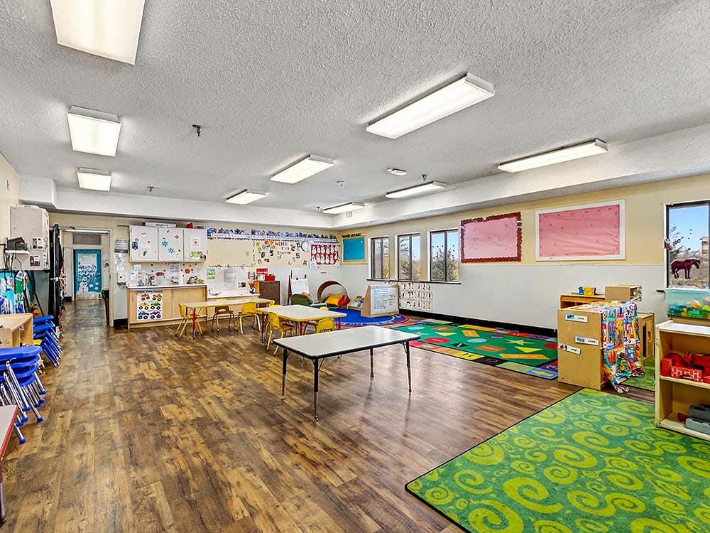 An empty classroom with small tables and chairs, colorful rugs, and decorated walls