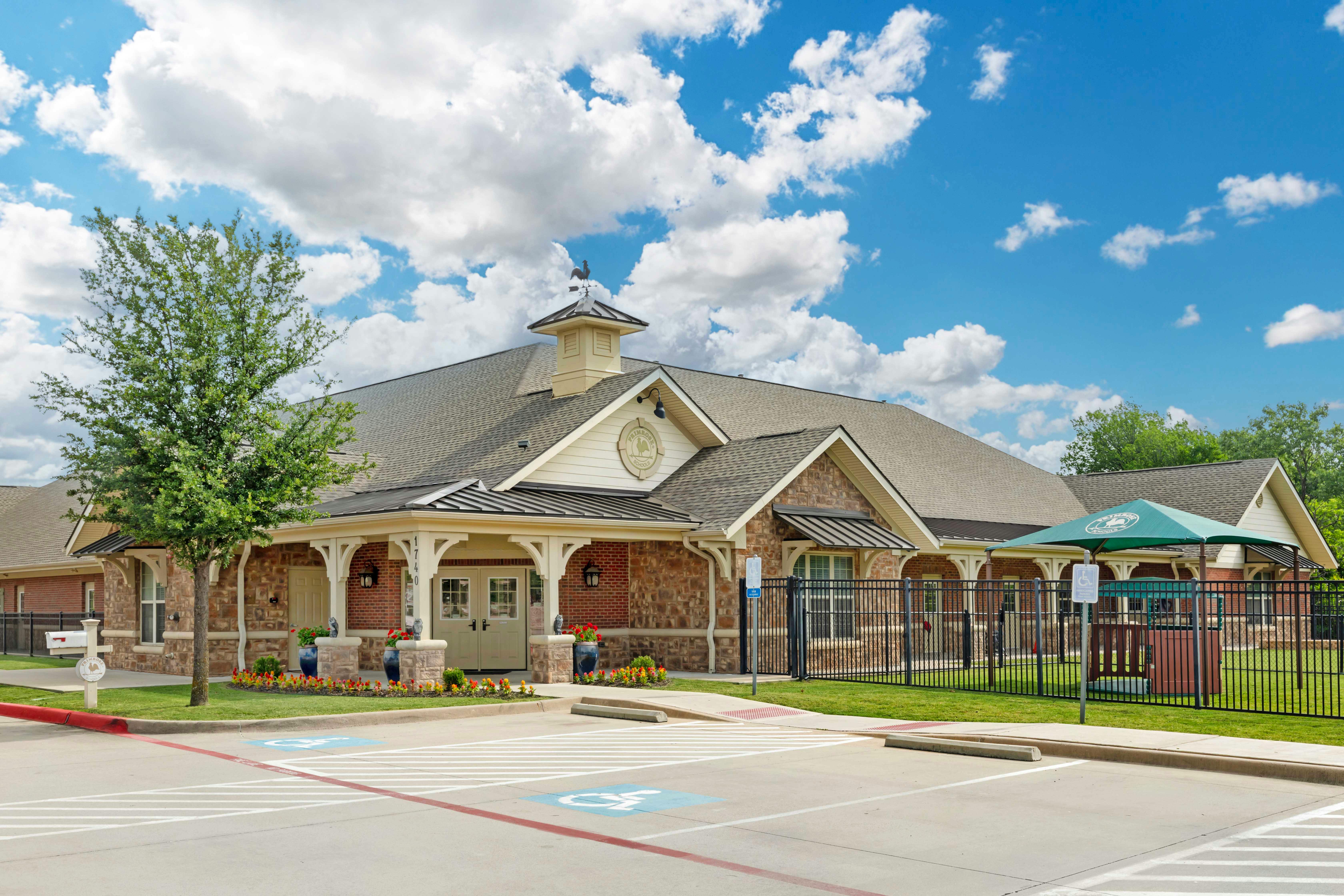 Front exterior view of a brick and stone building with a small tree and parking lot