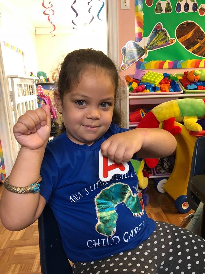 Child in a classroom holding up a letter A