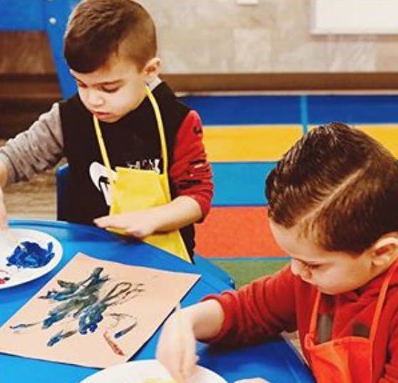 Two children wearing aprons painting at a table