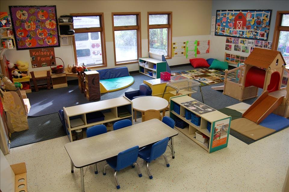 children's classroom with small tables and chairs, play mats, and a play structure with a slide