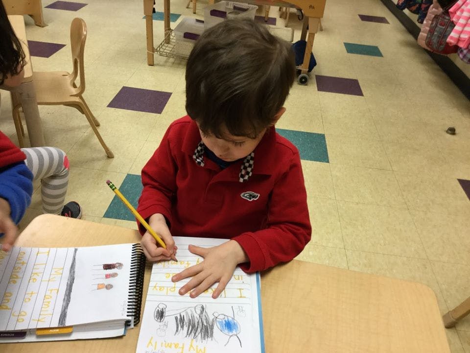 Child drawing in a notebook with a pencil in a classroom