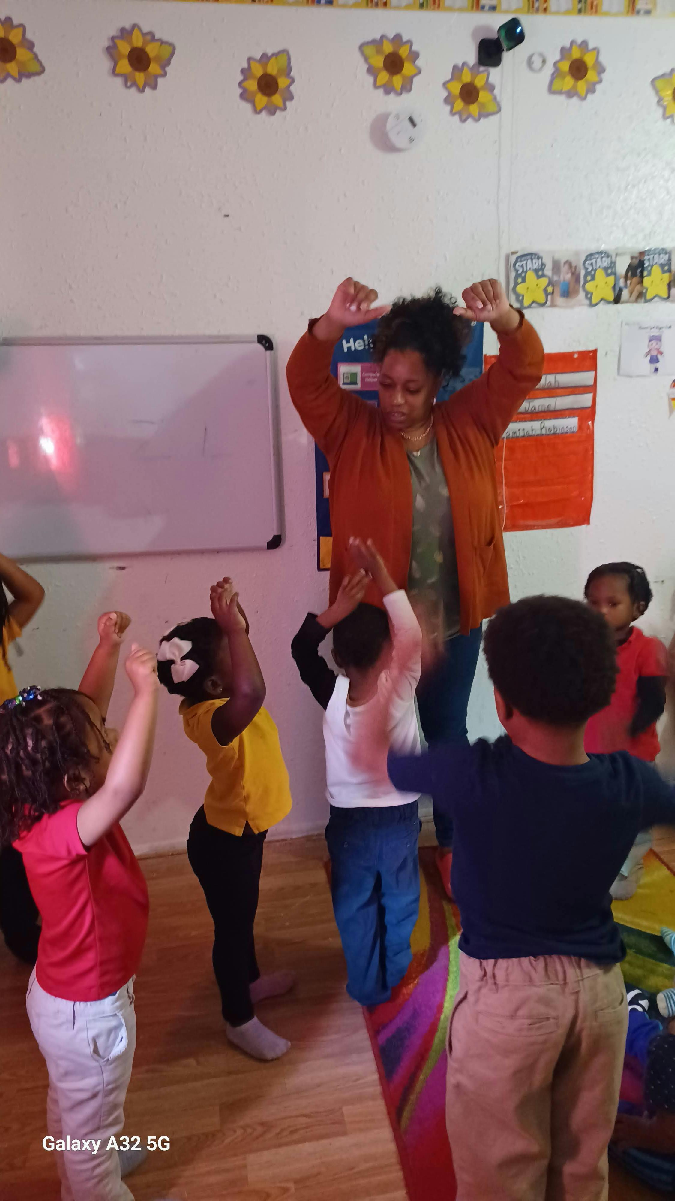 Group of children and one adult performing arm exercises in a classroom