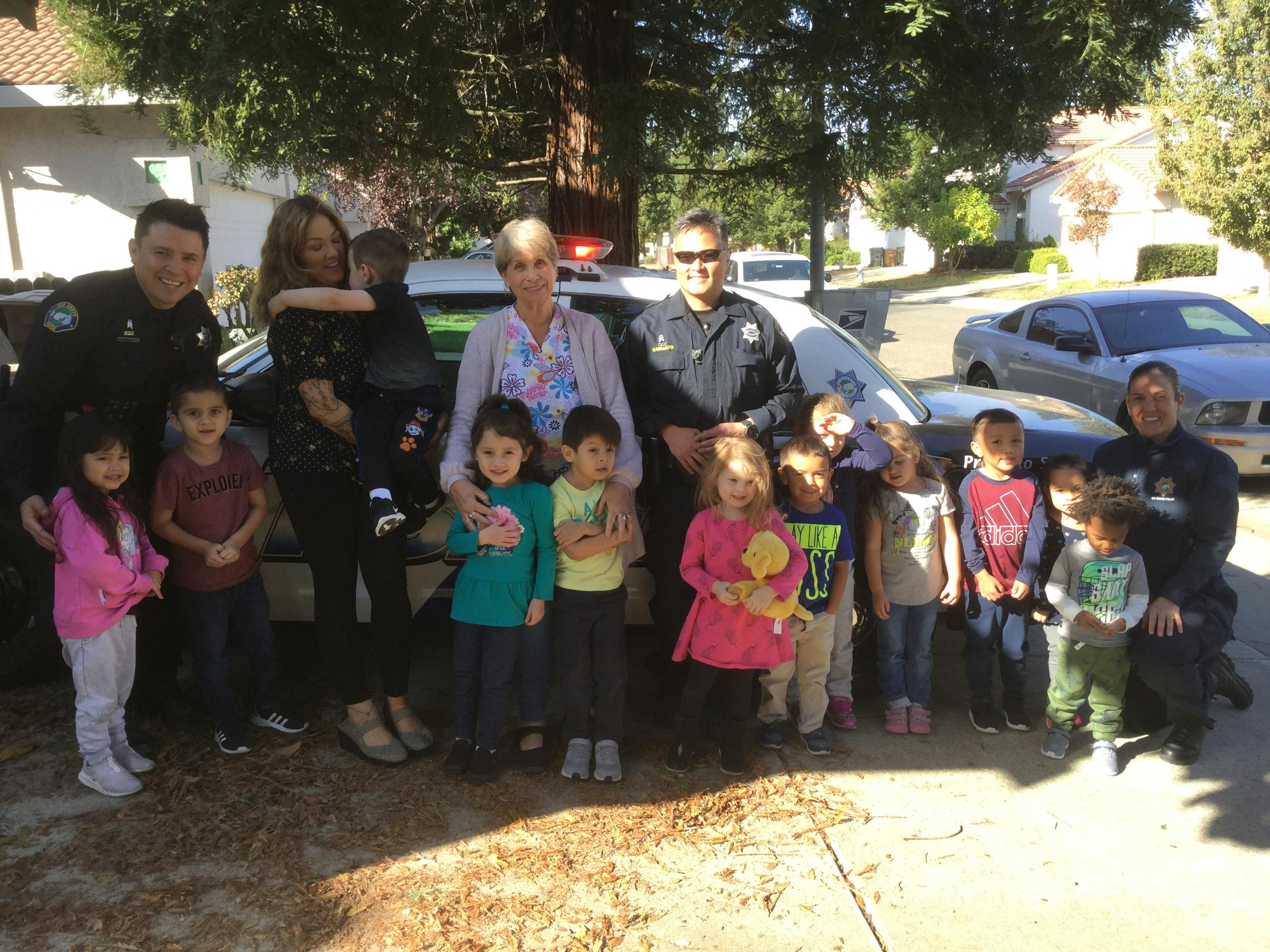 Two people in uniform and two adults with a group of children in front of a vehicle