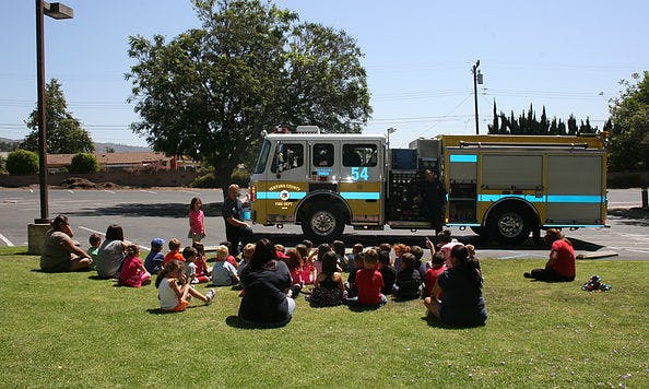 Children and adults sitting on grass in front of a fire truck
