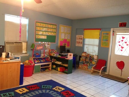 Classroom with a blue rug, shelves of toys, and educational posters on the walls