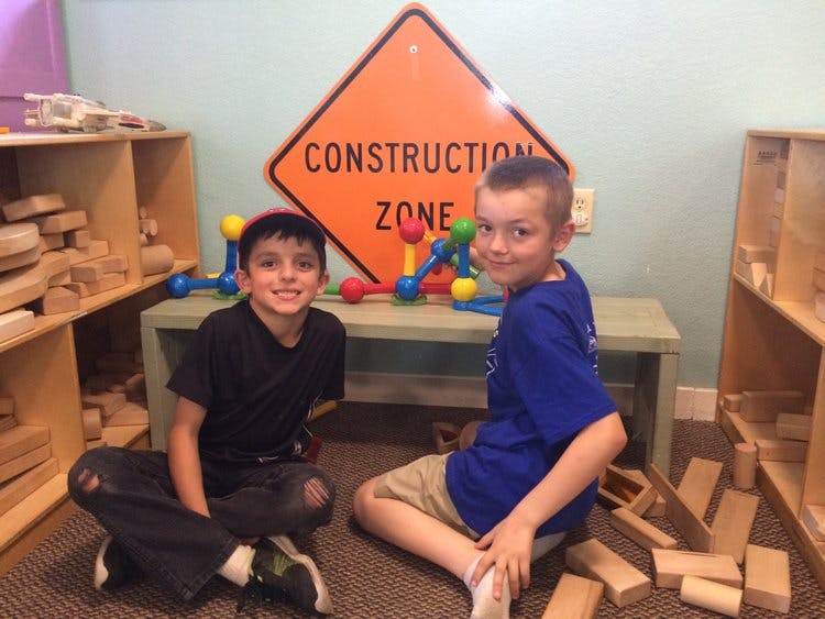 Two children sitting on the floor in front of a "Construction Zone" sign