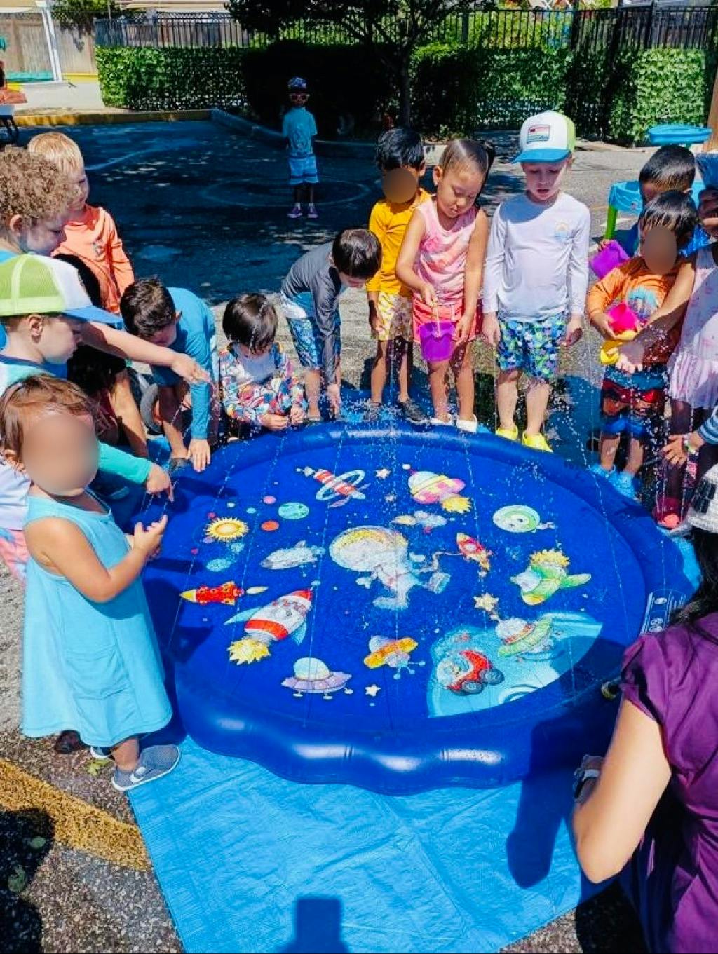 Children gathered around a blue inflatable pool with water toys