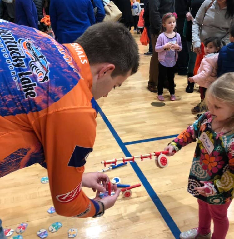 Person in orange shirt helping a child with a toy