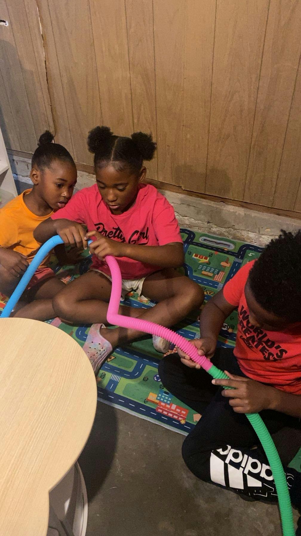 Three children playing with colorful pop tubes on tubes