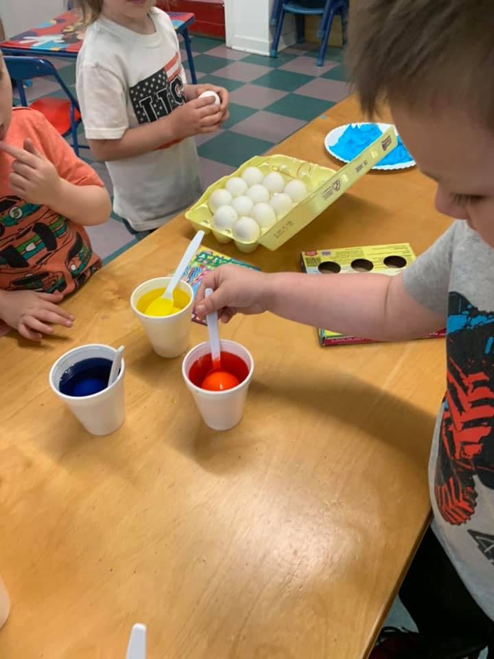 Child dipping an egg into a cup of red dye
