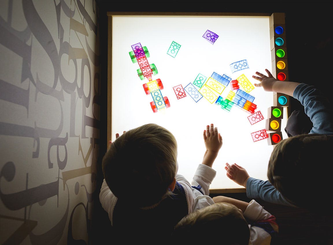 Children playing with colorful translucent blocks on a light table