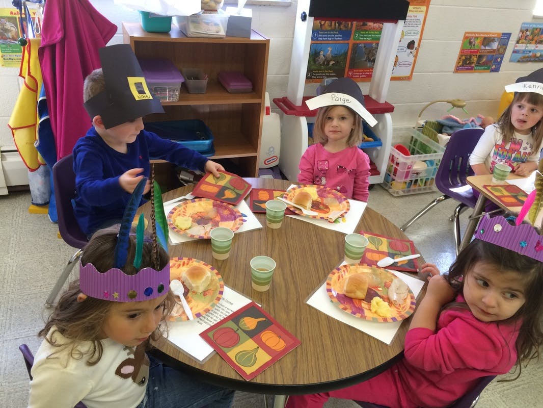 Children in hats sitting around a table with plates of food