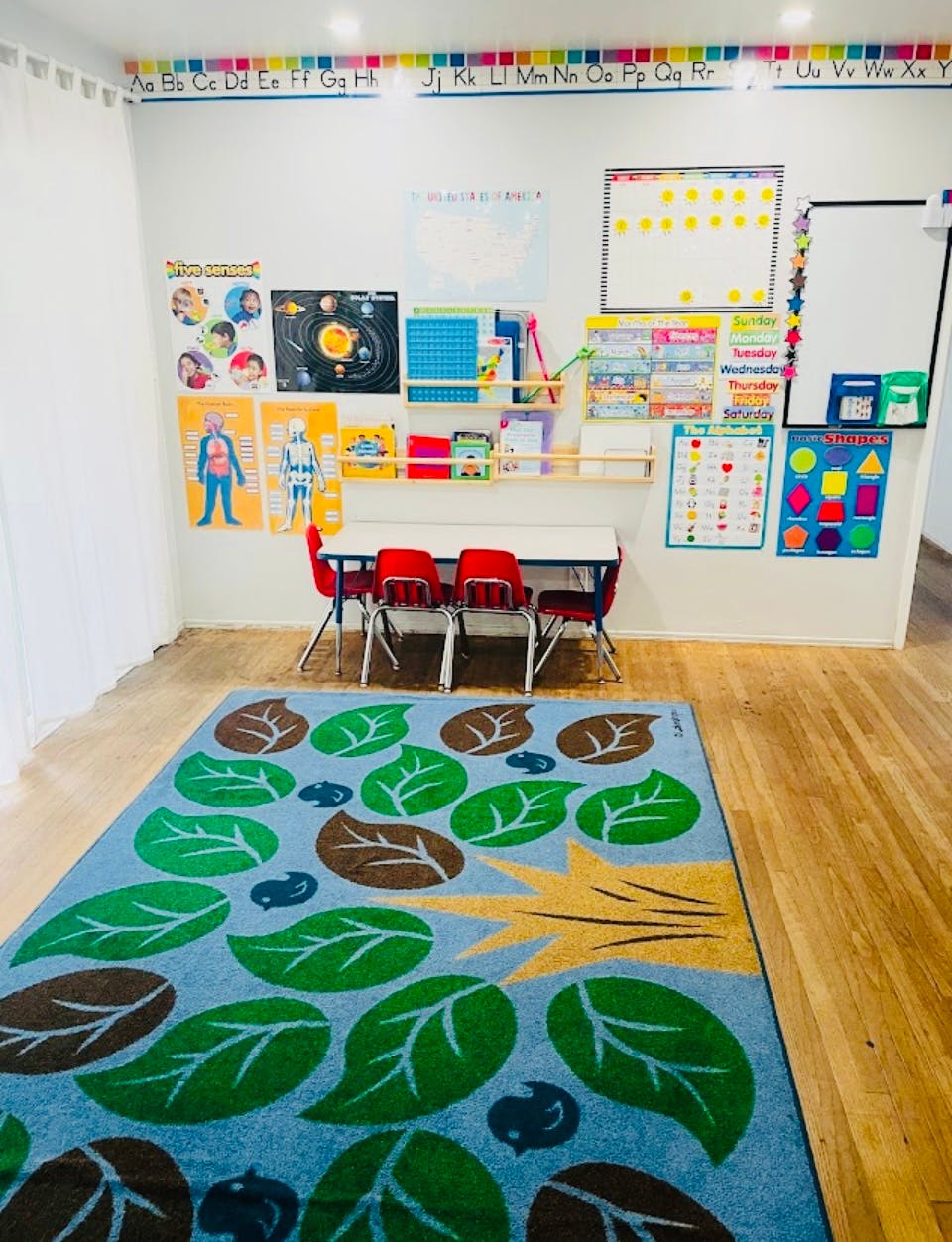 Classroom with educational posters, small table, chairs, and a leaf-patterned rug