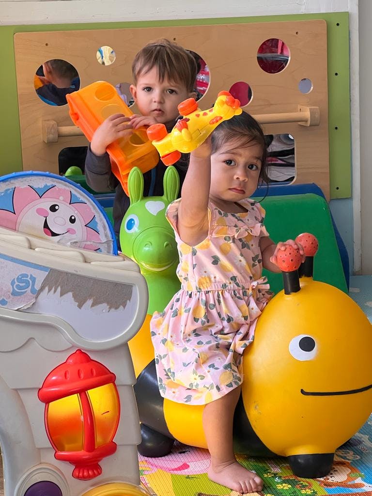 Two children playing with toys, one holding a yellow toy, the other on a yellow ride-on toy