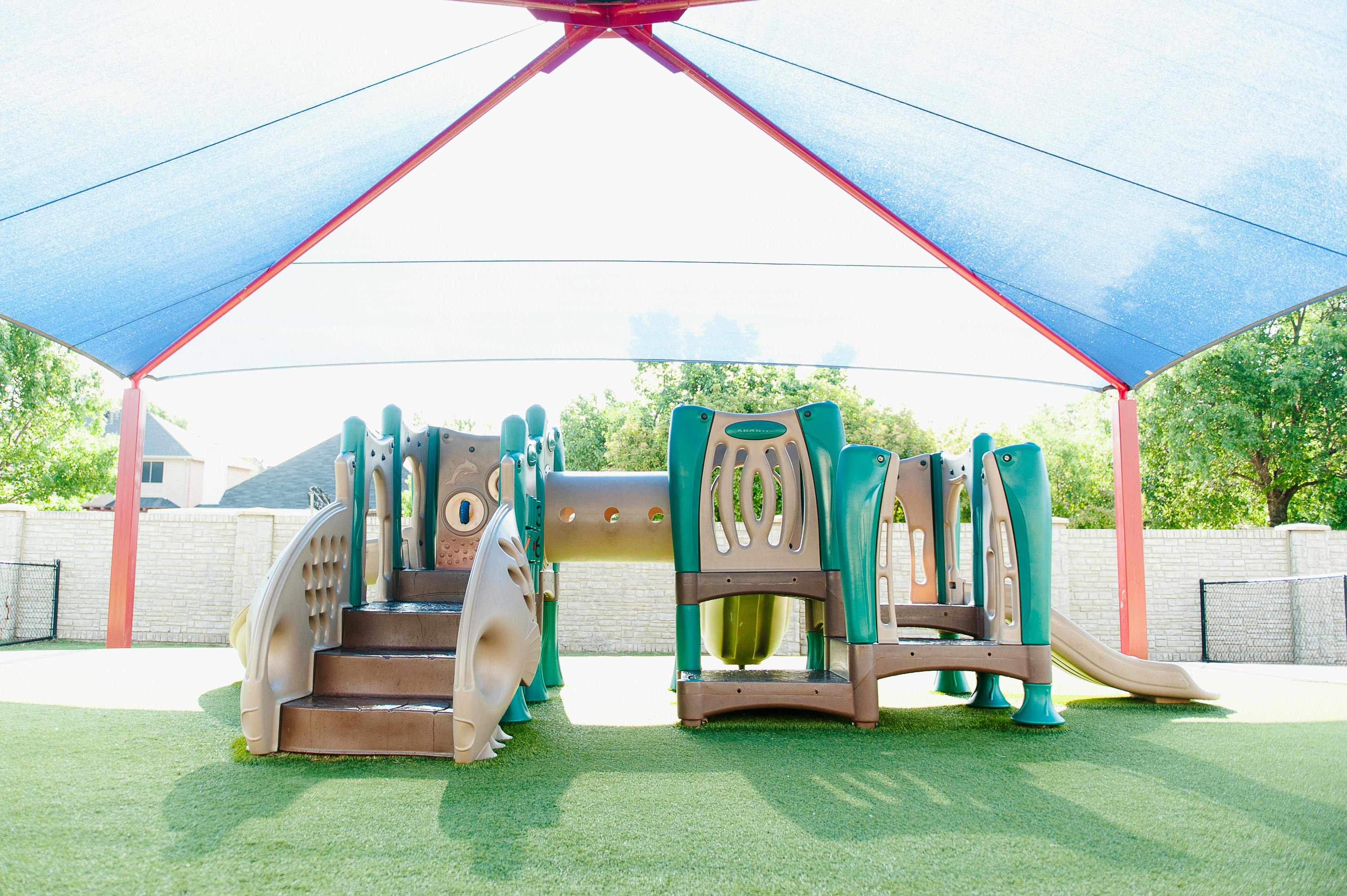 Playground structure with slides and steps under a blue shade canopy