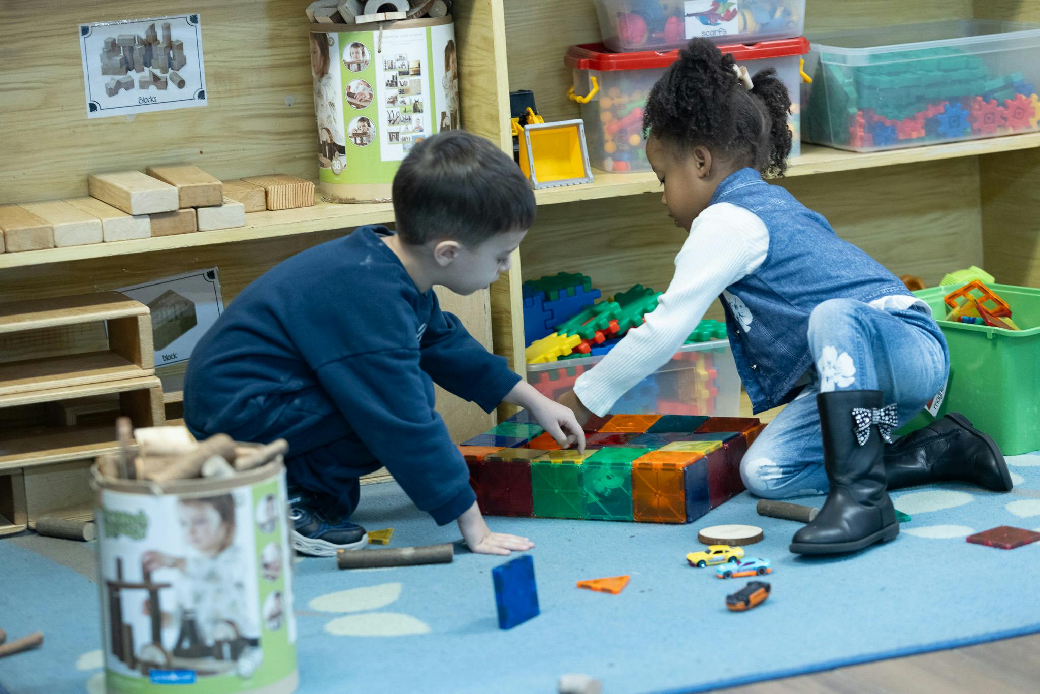 Two children playing with colorful blocks on the floor in a classroom