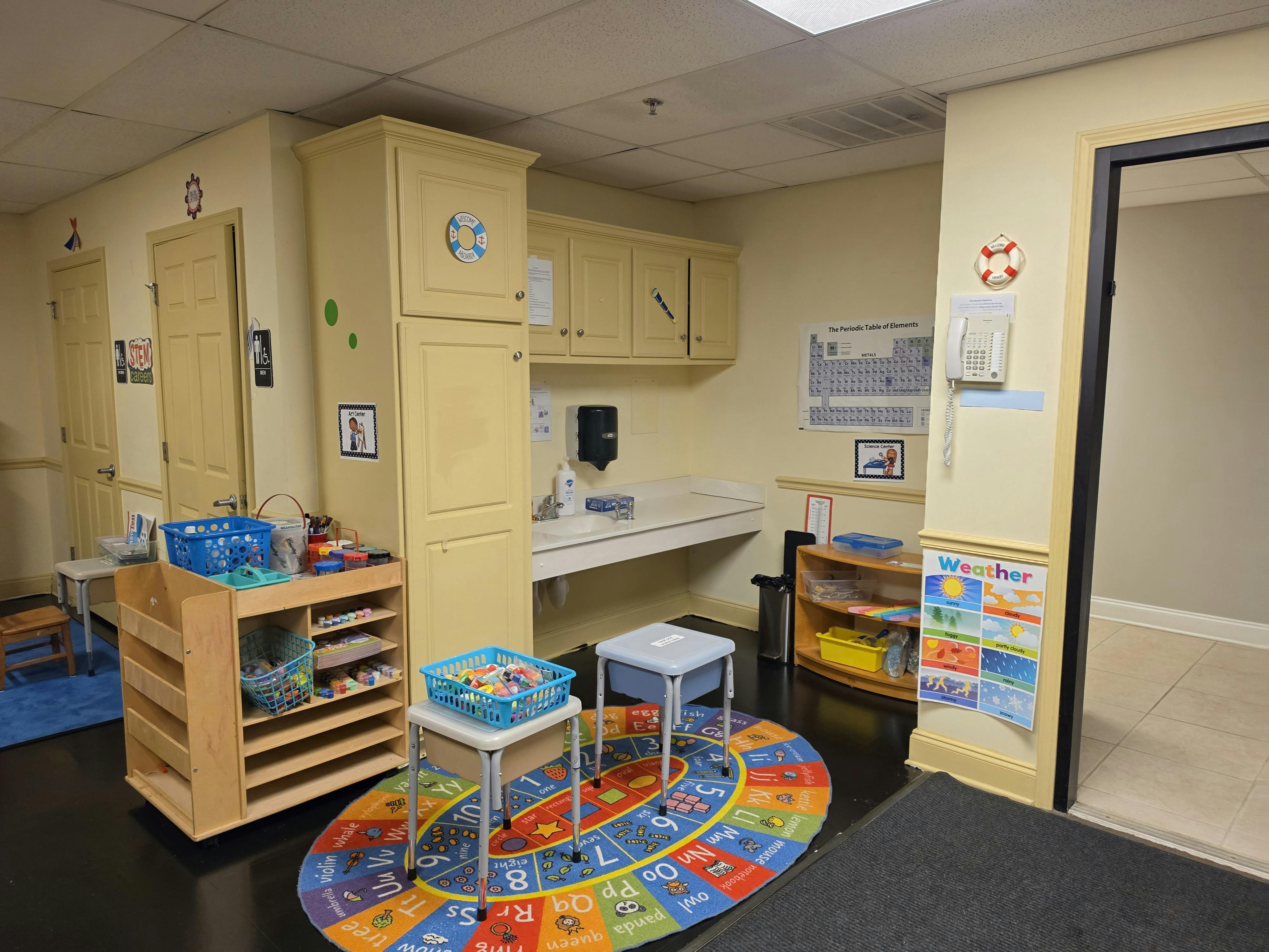 Classroom with child-sized furniture, a Periodic Table of Elements, and a Weather chart