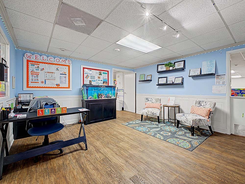 Classroom with a desk, two armchairs, an aquarium, and a welcome board