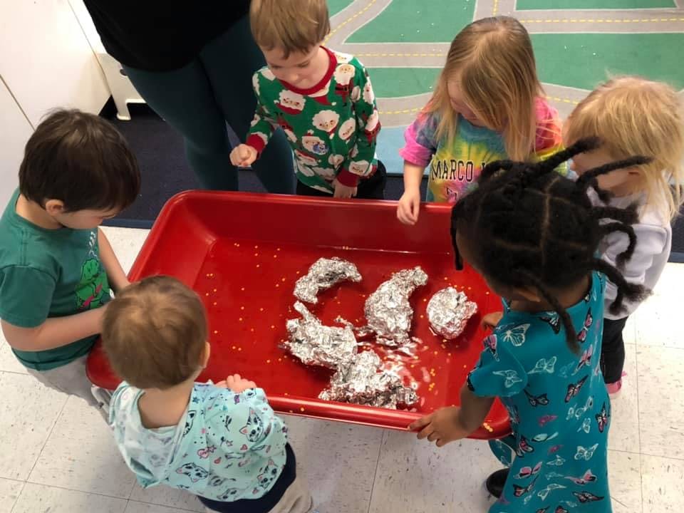 Children gathered around a red bin with foil-wrapped items
