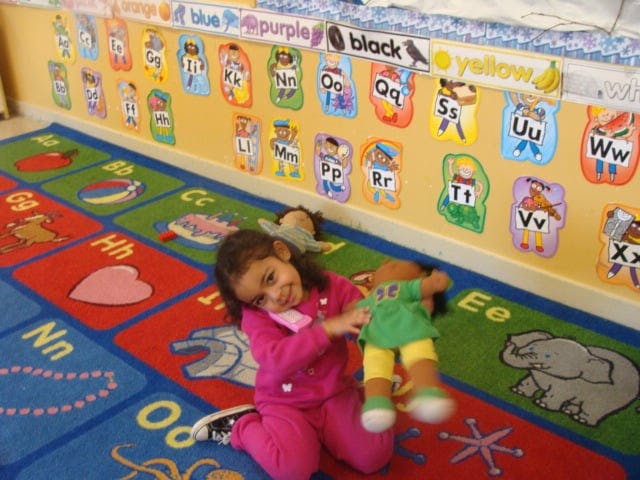 Child playing with a doll on an alphabet rug in a classroom