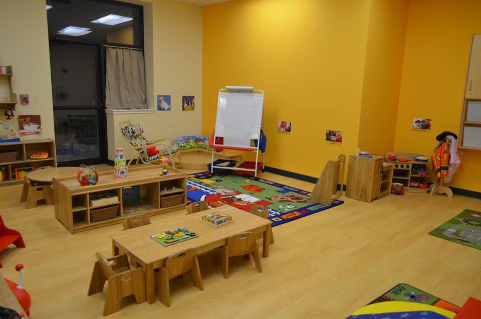Empty classroom with small wooden tables and chairs, colorful rugs, and a whiteboard