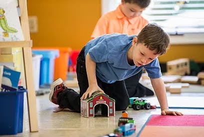 Child playing with a toy barn on the floor