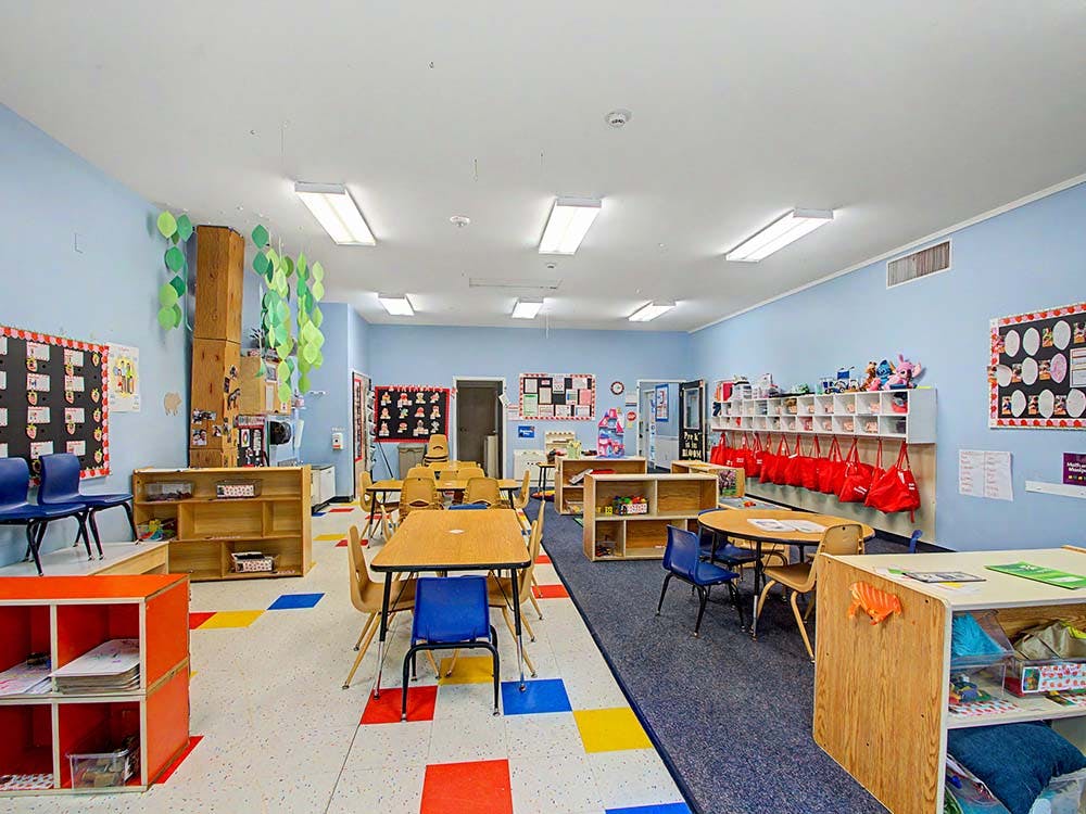 Empty classroom with small tables and chairs, shelves, and decorations