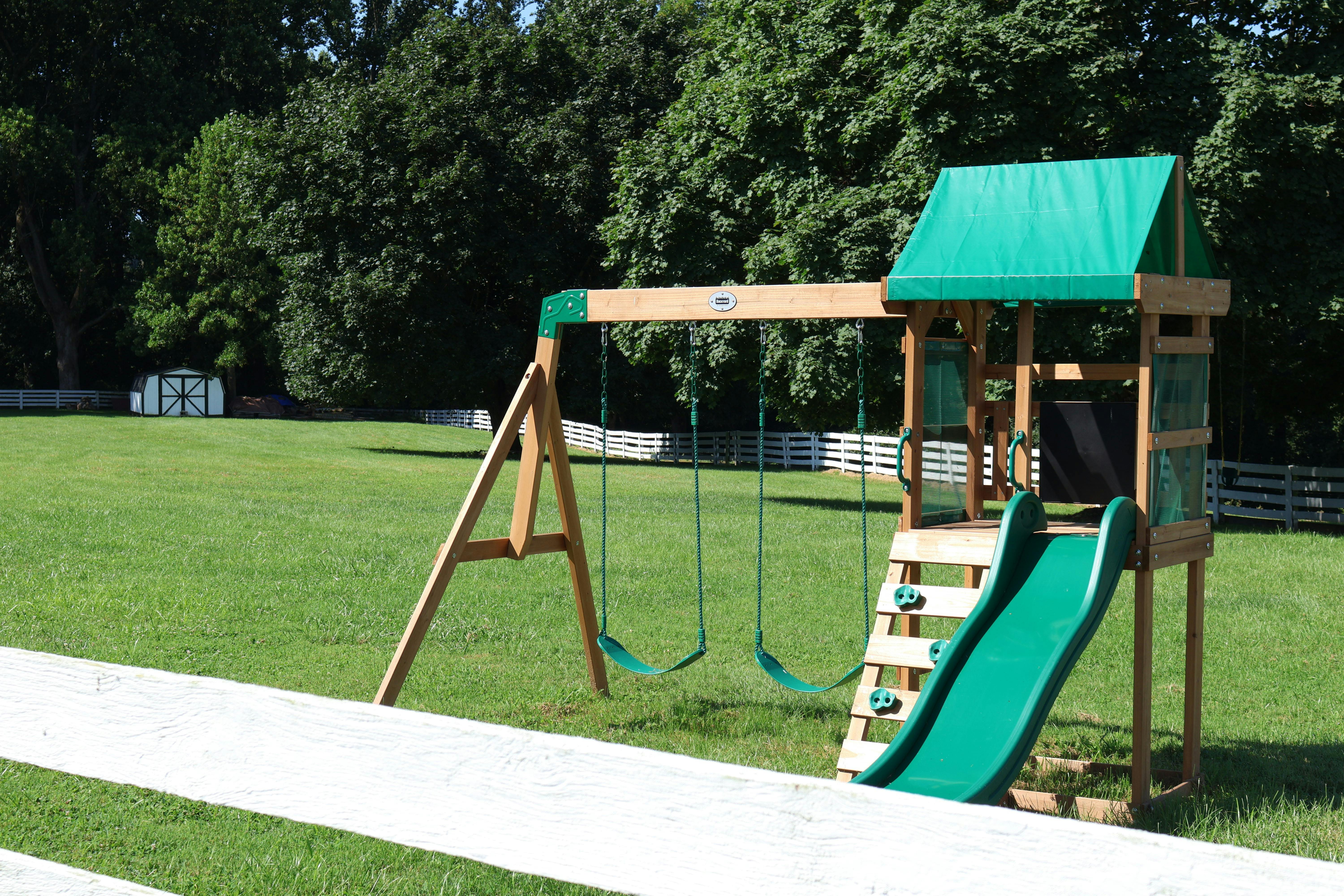 Wooden playset with swings and a slide on a grassy lawn