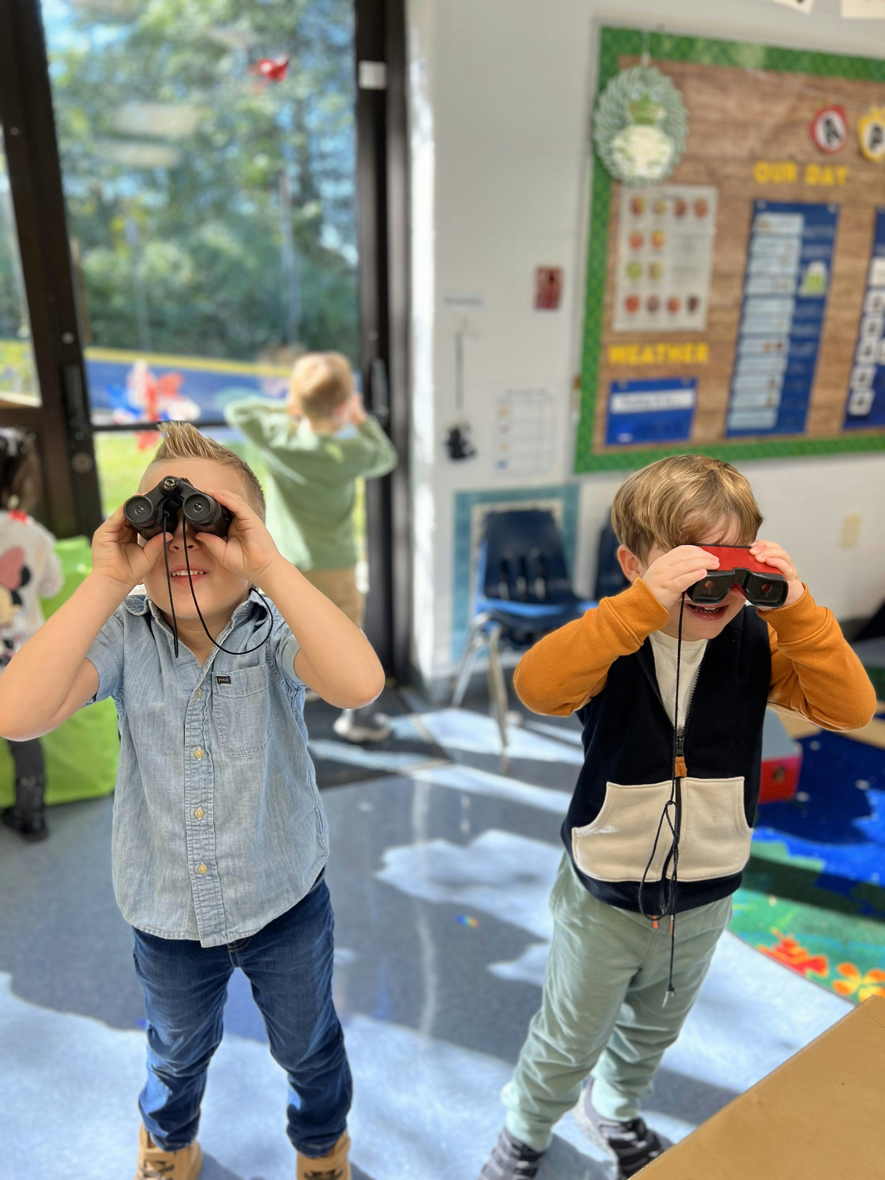Two children looking through binoculars in a classroom