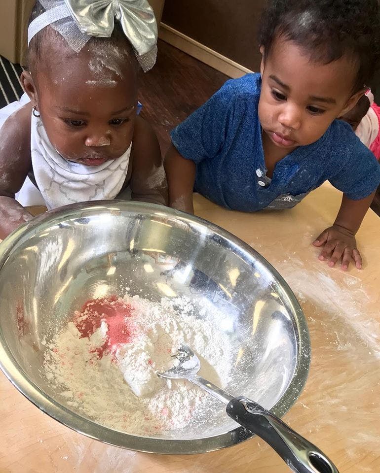 Two children looking at a bowl of flour and red powder