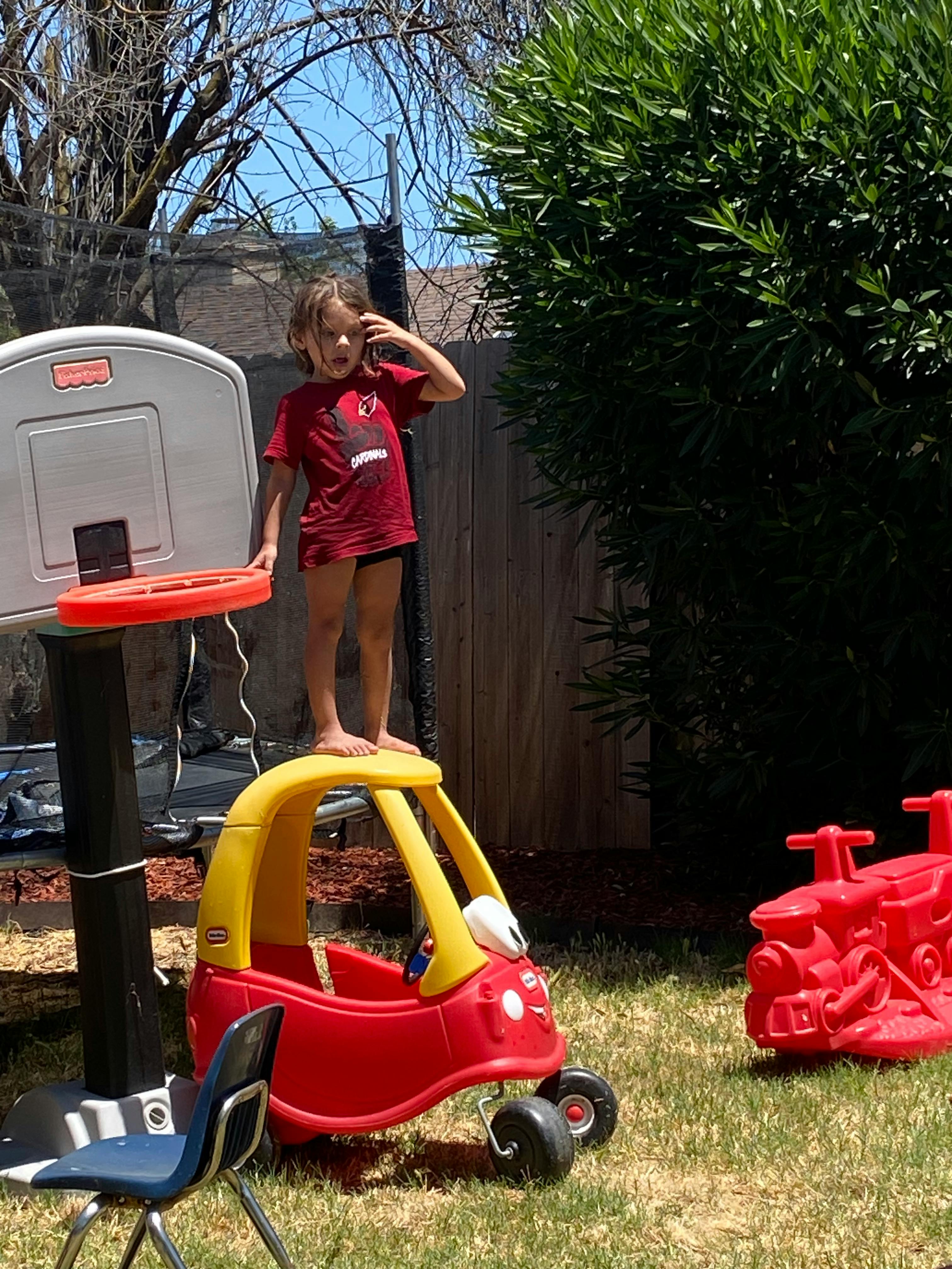Child standing on a toy car next to a basketball hoop