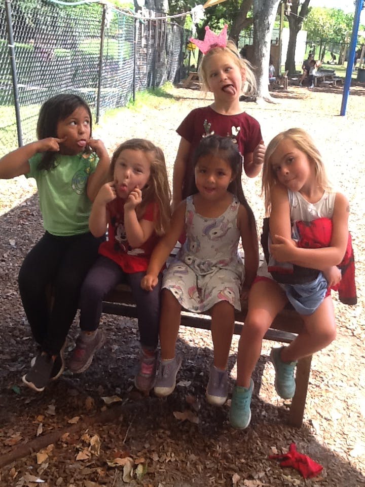 Five children making silly faces while sitting on a bench