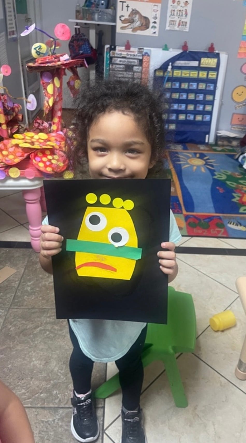 Child holding a handmade paper monster craft in a classroom