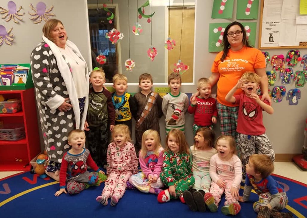 Two adults with a group of children in pajamas in a classroom