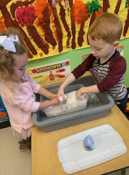 Two children washing items in a bin of soapy water