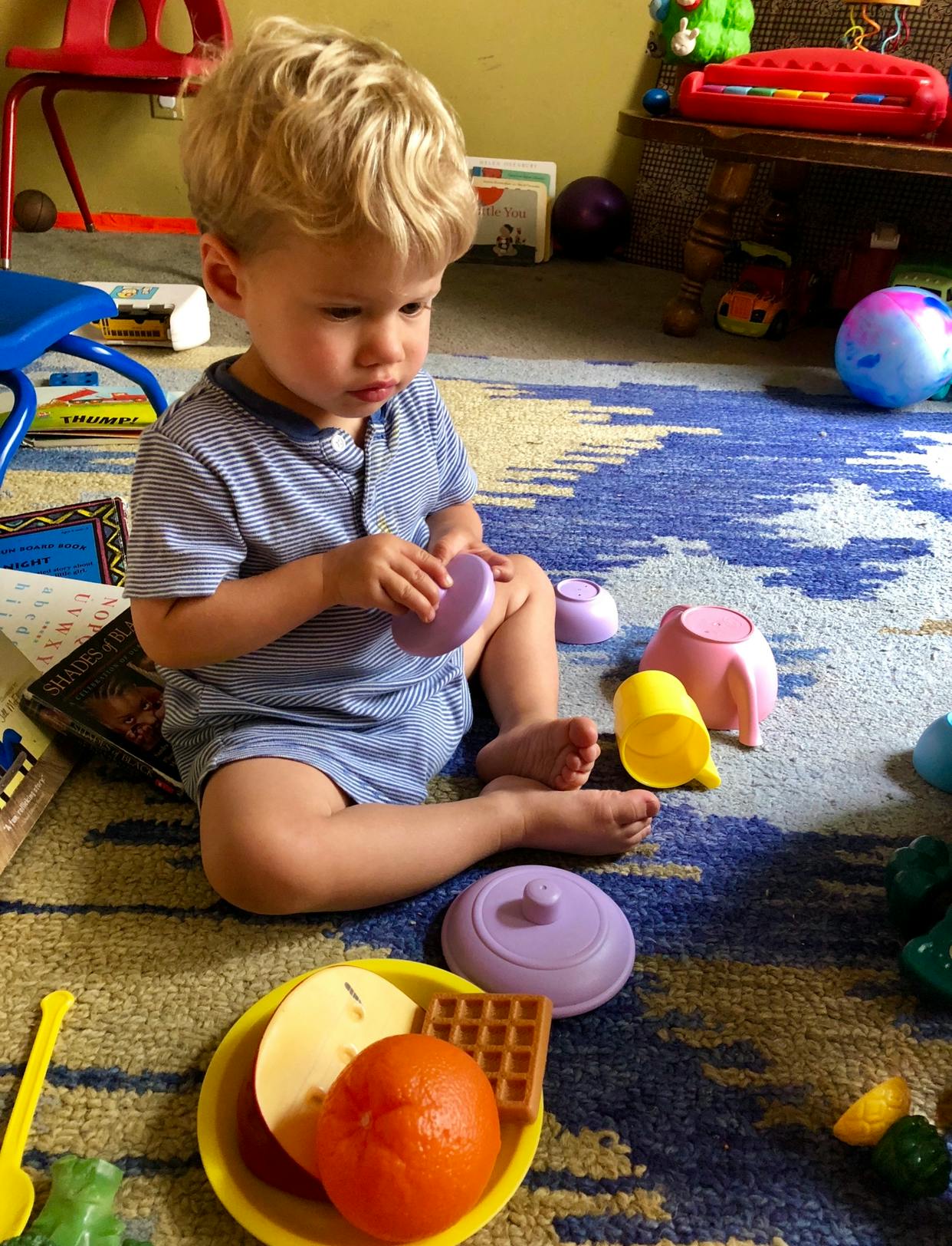 Child playing with toy food and dishes on a rug