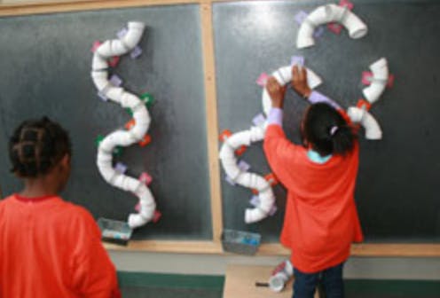 Child arranging white pipe pieces on a dark board