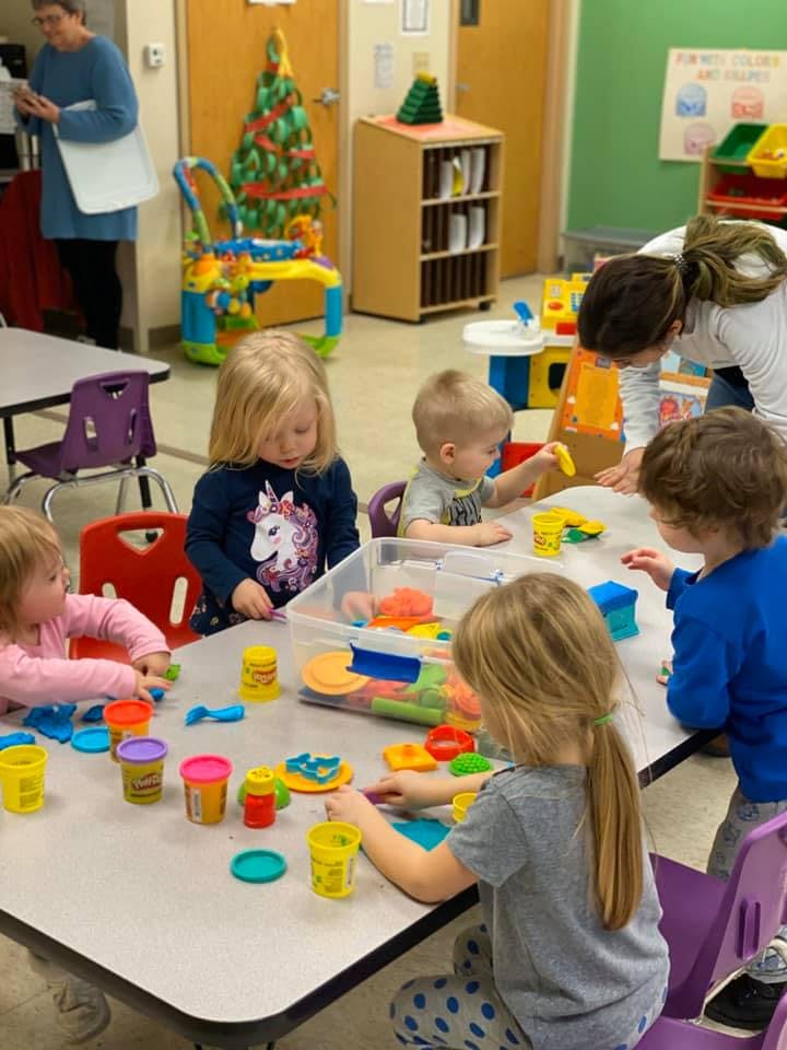 Children playing with colorful modeling clay at a table in a classroom