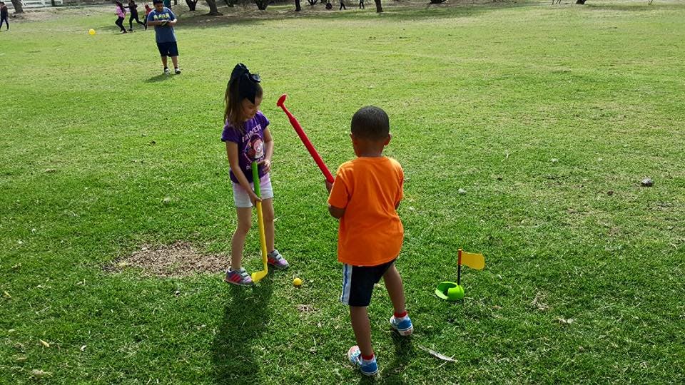 Two children playing mini golf on a grassy field