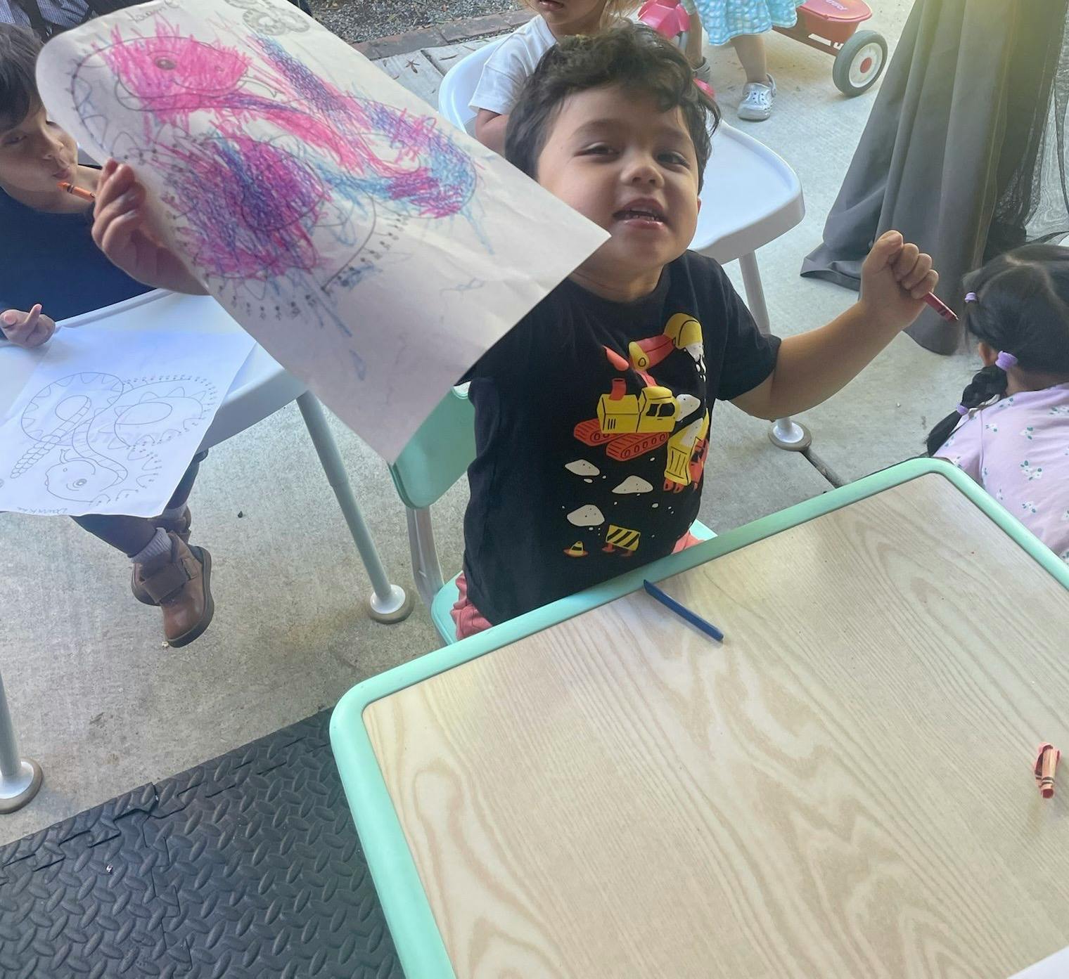 Child holding up a drawing while holding a crayon