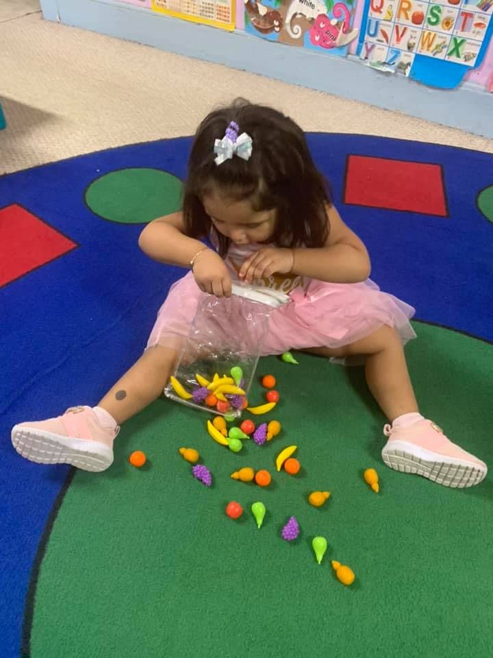 Child playing with colorful fruit and vegetable toys on a rug