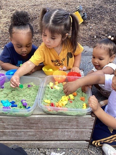 Children playing with kinetic sand and toys in a wooden sandbox
