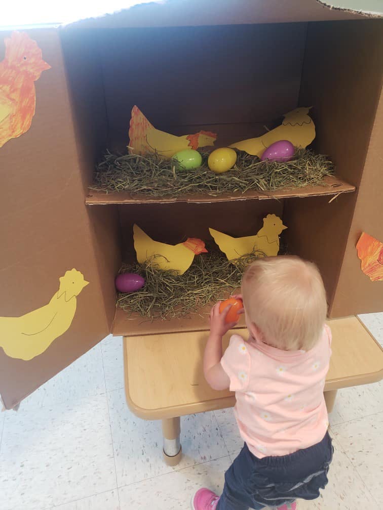 Child playing with a cardboard chicken coop with paper chickens and eggs