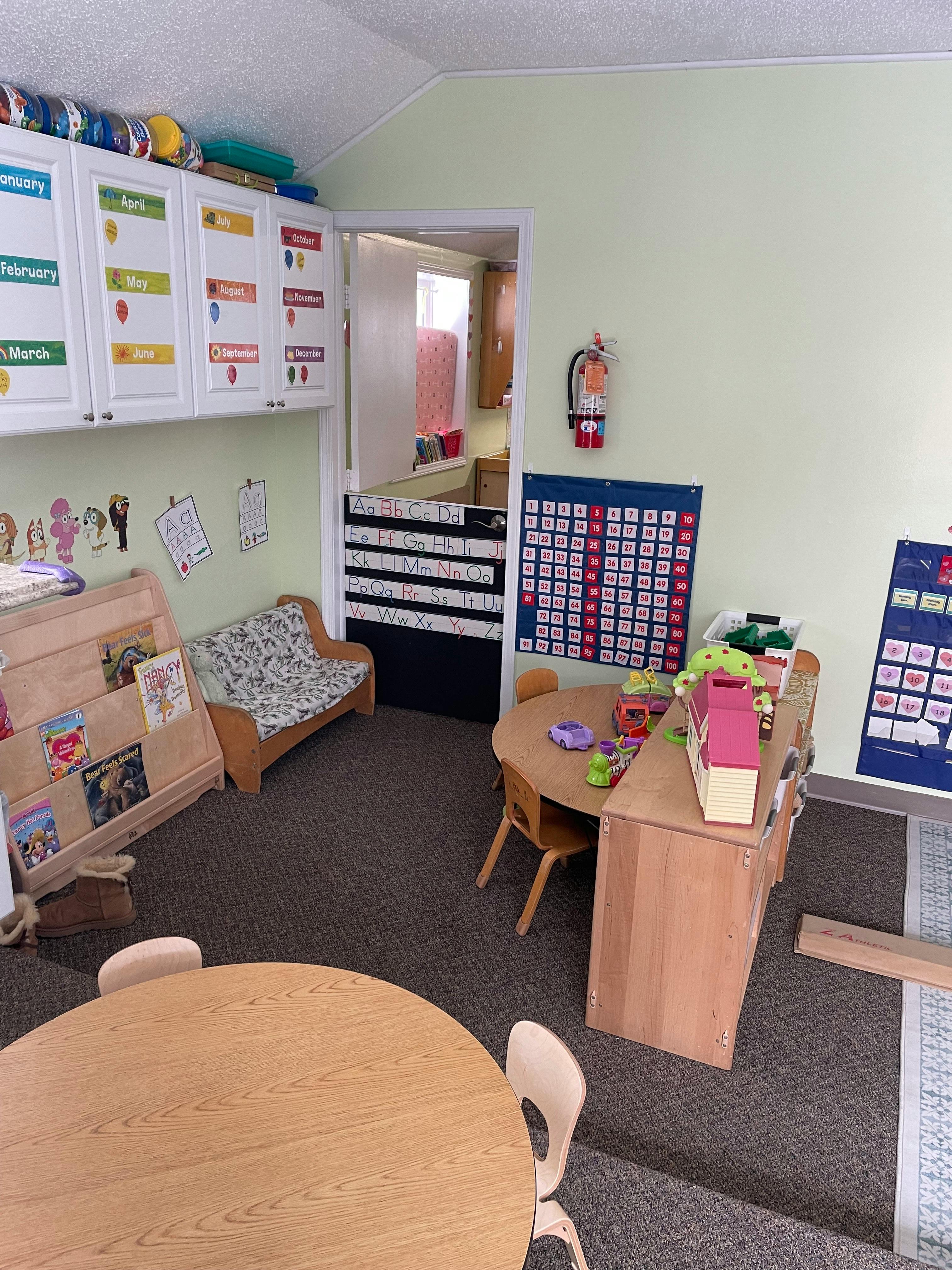 A classroom with small tables and chairs, a bookshelf, and wall calendars