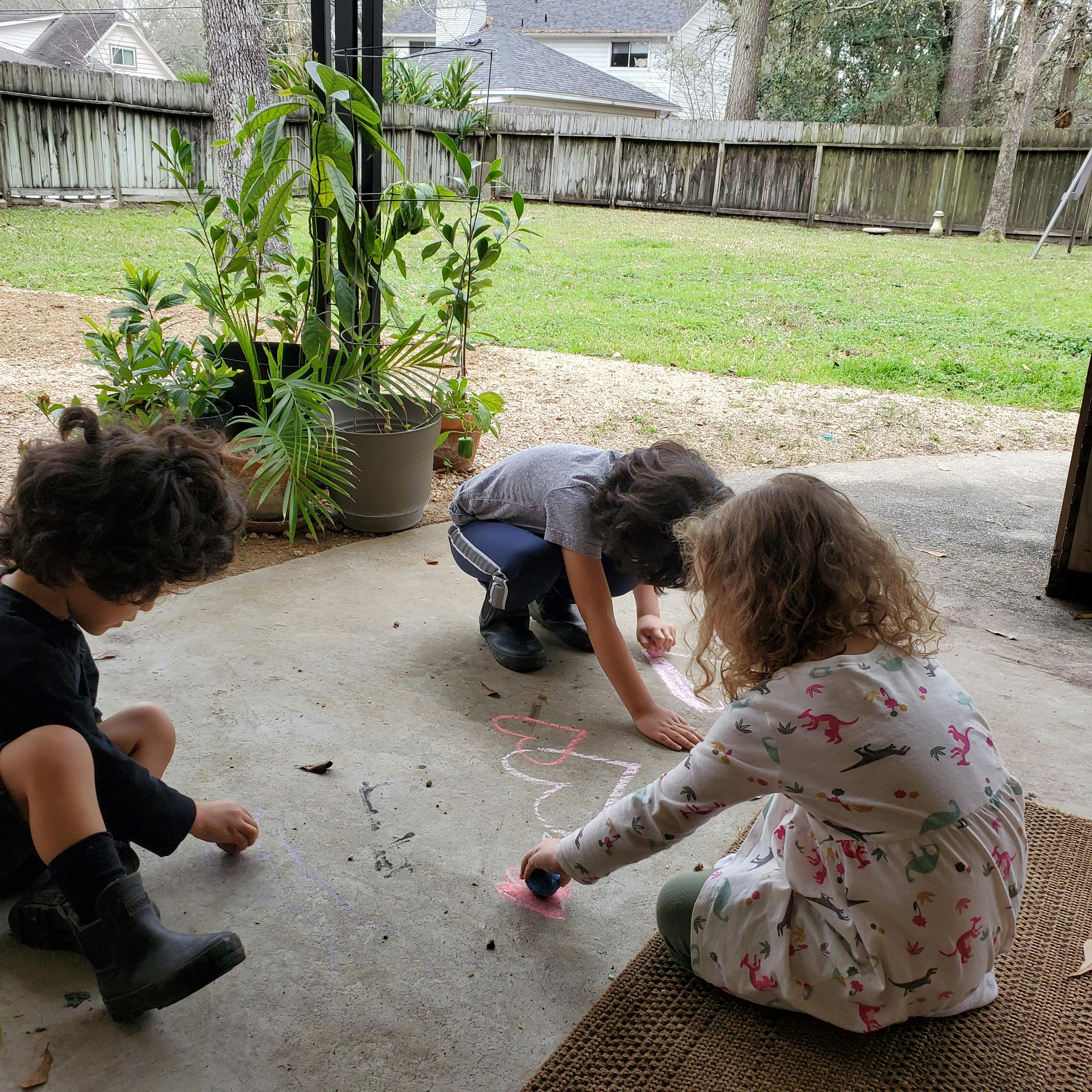 Three children drawing with chalk on a patio